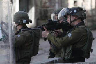 An Israeli soldier aims his gun at Palestinian protesters during clashes in the West Bank city of Hebron, on March 1, 2022