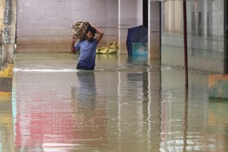 A man with his belongings crosses a flooded road at Sarjapur