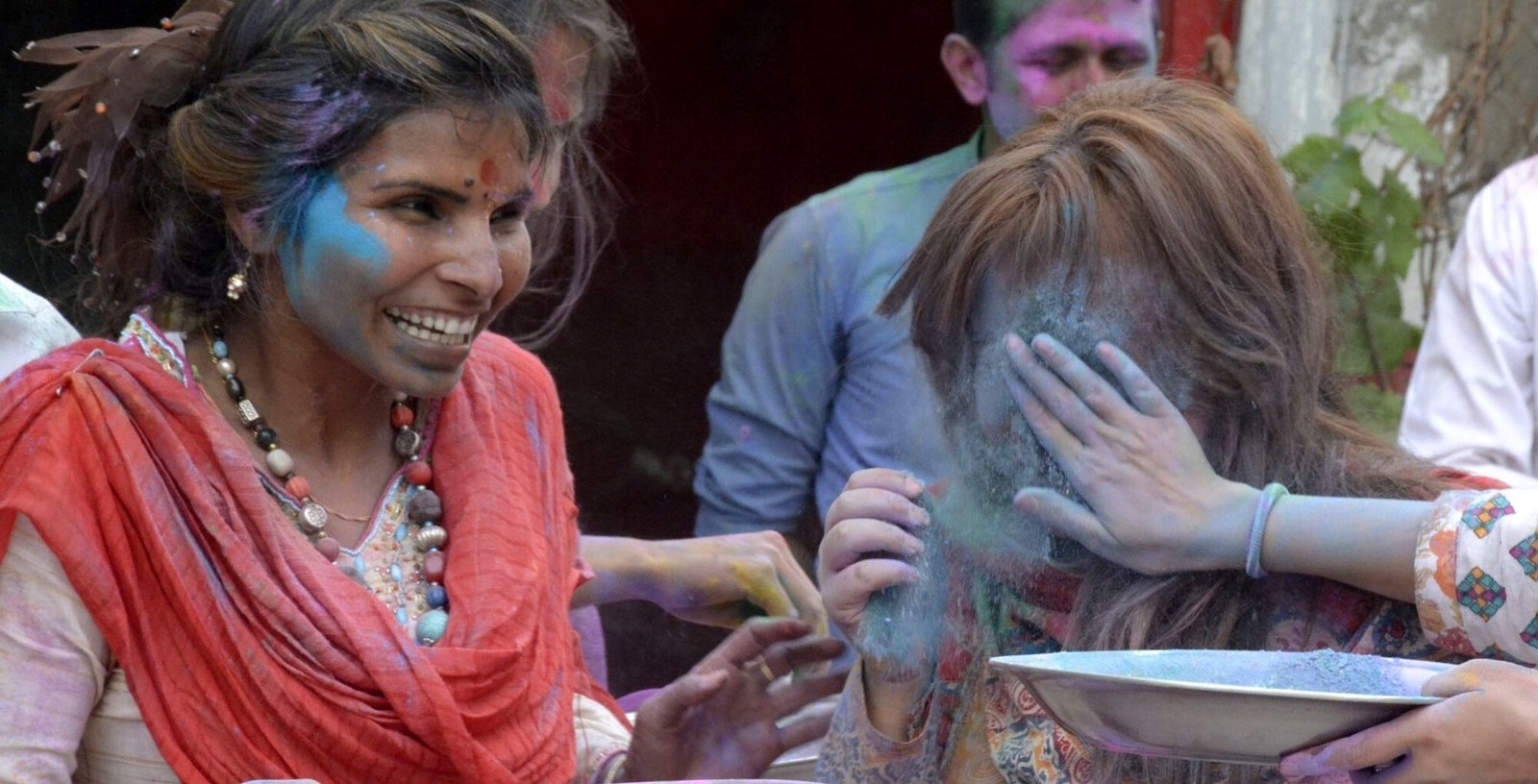A Pakistani Hindu scatters color powder on a woman's face