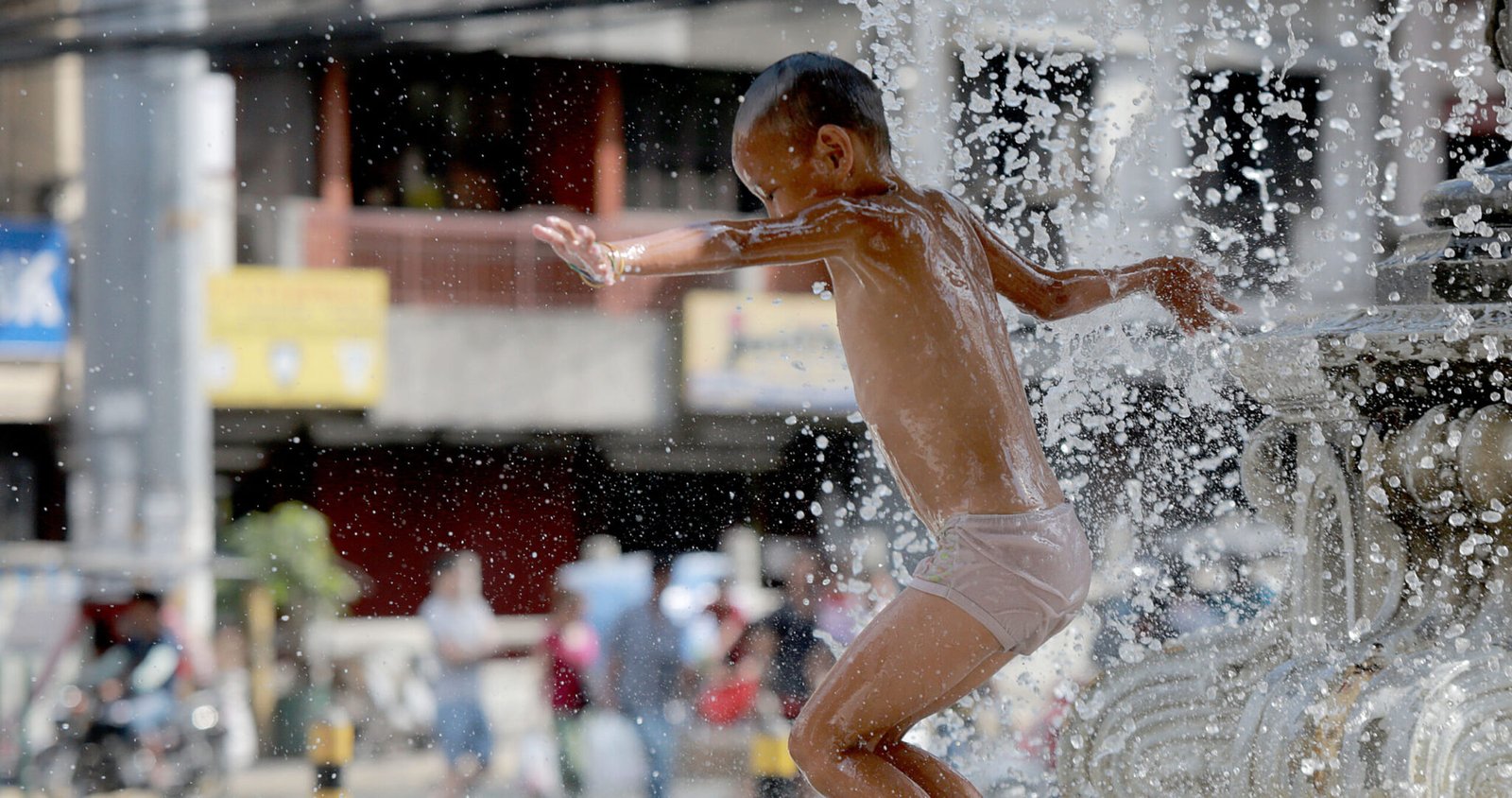 A boy frolics at a fountain to cool off from the summer heat